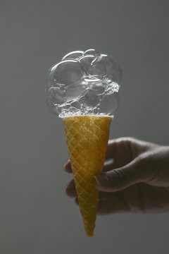 Hand holding a soap bubble ice cream on a grey background.