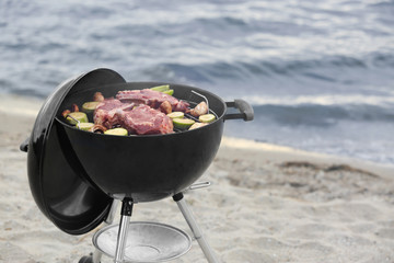 Barbecue grill with tasty steaks and vegetables on beach - Powered by Adobe