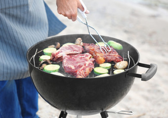 Man cooking tasty steaks and vegetables  on barbecue grill, closeup