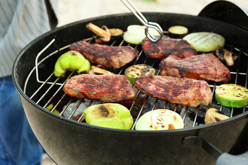 Tasty steaks and vegetables cooking on barbecue grill, closeup