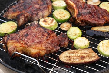 Tasty steaks and vegetables cooking on barbecue grill, closeup