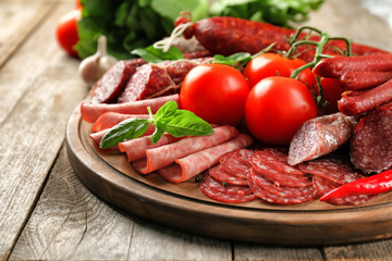 Delicious sliced sausages with vegetables on wooden board