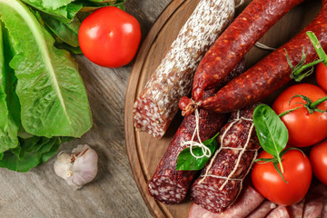 Delicious sliced sausages with vegetables on wooden board