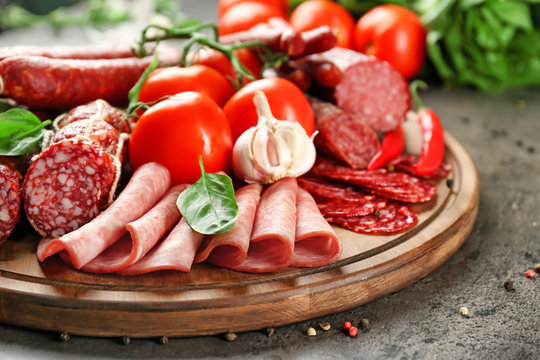 Delicious sliced sausages with vegetables on wooden board
