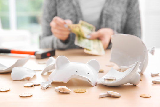 Broken piggy bank with coins and blurred woman on background
