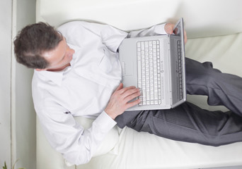 view from the top.man working on laptop lying on a sofa.