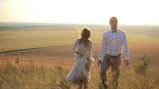 beautiful guy and girl are walking along the field for a day's sake against the backdrop of a picturesque rural landscape. Wedding beautiful young couple walking on the background of meadows