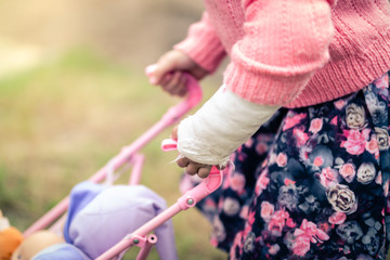 Girl with Broken Arm in Cast Playing with Doll in Toy Pushchair