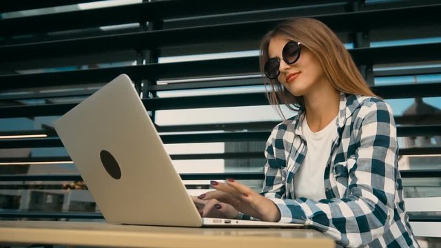 Attractive student girl works with laptop computer before modern building wall, slowmotion