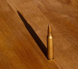 Fototapeta na wymiar A single .223 bullet on a wooden table with the sunlight casting a shadow behind it