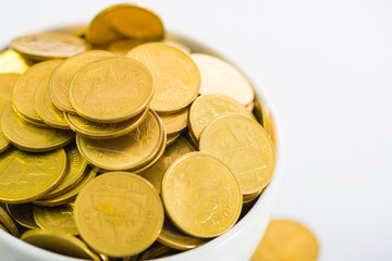 Golden coins in white cup of coffee on the white background.