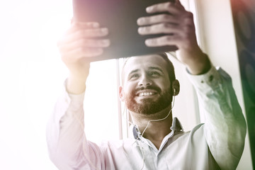 Naklejka premium smiling businessman with digital tablet and earphones calling with video conference