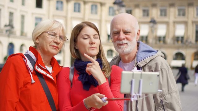 Young daughter taking selfie photo on mobile with her senior parents on vacation trip in Paris in Place Vendome. Happy family enjoying vacation.