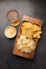 Beer in glasses closeup on the concrete table. Beer and snacks are chips and nachos with cheese souce top view. Drink and snack for the football match or party