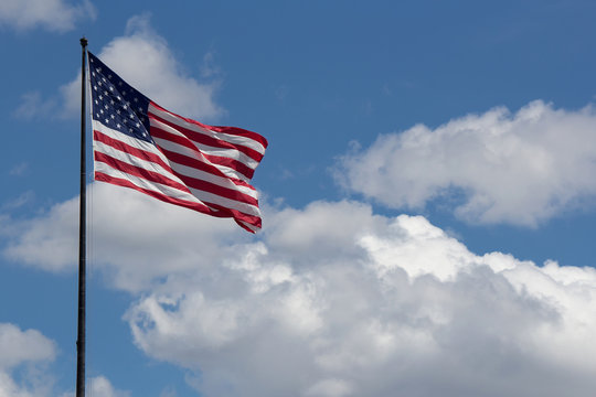Flag of United States of America (USA) waving in the wind with blue sky and clouds on background