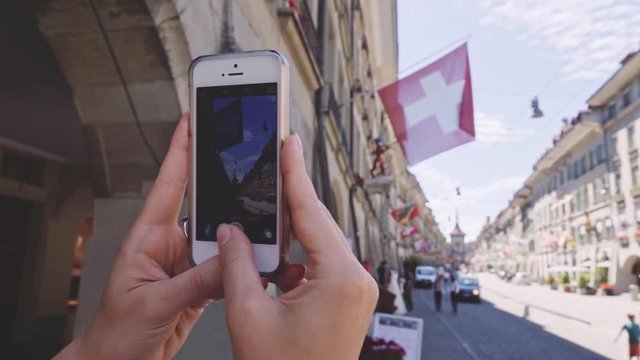 Tourist Woman Taking Photographs in Bern, Switzerland, CLOSE UP. SLOW MOTION 240 fps. Female Hands making a Picture of Kramgasse with a Smartphone in the Old Town of Bern in summer. Travel concept 