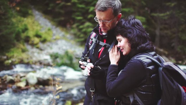 Adult Man and Woman Hikers Looking Through Photos They Took with Digital Camera. SLOW MOTION. Mature Tourists Couple enjoying mountain and forest nature. 