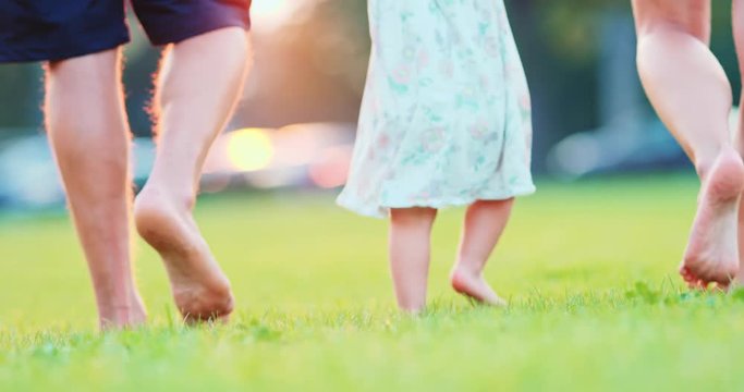 Little baby learns to walk. Family feet Close Up. First Steps. SLOW MOTION 120 fps, 4K. Parents are teaching their child to do the first steps on a green grass. Happy childhood and Parenthood concept