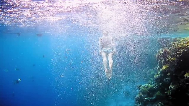 Beautiful woman dive underwater in snorkeling diving mask into clear blue sea water. Tropical underwater reef diving. Woman with a good figure slow motion shot.