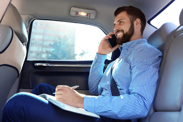 Handsome man with smartphone on backseat of car
