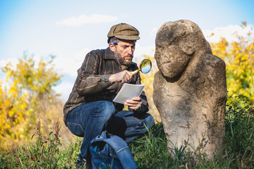 Scientific historian examines through magnifying glass stone sculpture on mound
