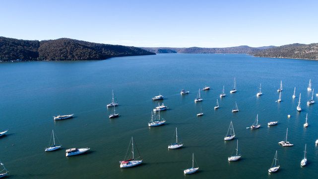 Aerial view of boats moored on Hawkesbury River, Brooklyn, Australia with blue water and headland in background