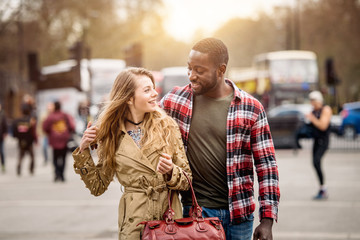 Multiracial couple walking in London. He is middle eastern, she is caucasian, both are smiling and looking each other. They could be friends or in a relationship. Lifestyle and love concepts.