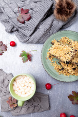 Grey knitting gloves, cake and cup of coffee with marshmallow on grey background. Top view. Copy space. Knitting yarn.