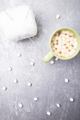 White knitting ball and needles in two cup of coffee with marshmallow on grey background. Top view. Copy space. Knitting yarn.