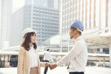 Fototapeta na wymiar Smart beautiful engineer shaking hands with handsome foreman. background city