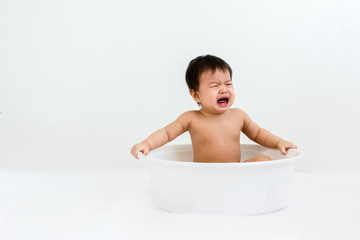 Portrait of a crying baby sitting in the basin for shower, indoors