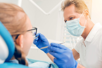 Friendly looking mature dentist checking teeth of teen client