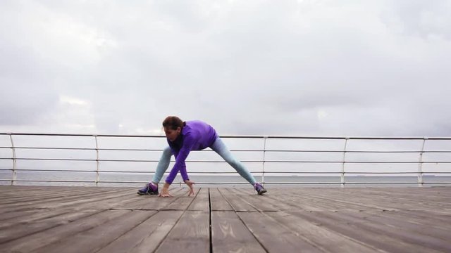 Young athletic woman stretching her legs before her training on the beach by the sea early in the morning. Training by the beach in summer
