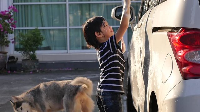 Asian child washing car in the garden with dog on summer day slow motion 