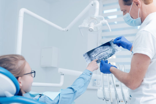 Male dentist showing x ray scan picture to little patient