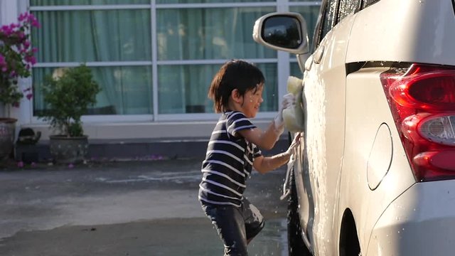 Asian child washing car in the garden with dog on summer day slow motion 