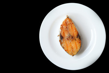 A grilled mackerel fish on white plate  over black background