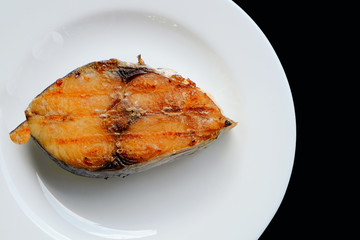 A grilled mackerel fish on white plate  over black background
