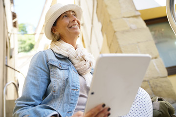 Senior woman sitting in town using digital tablet