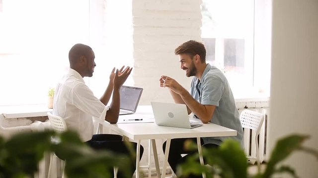 African american and caucasian businessmen talking in loft office, diverse colleagues joking laughing in friendly easygoing coworking atmosphere, good relations at workplace, making friends at work