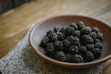 The blackberry in a ceramic bowl lies on a wooden table.