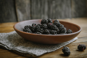 The blackberry in a ceramic bowl lies on a wooden table.