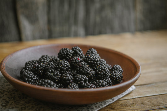 The blackberry in a ceramic bowl lies on a wooden table.