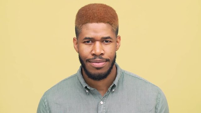 closeup african american guy with stylish haircut in blue skirt looking at camera smiling standing over yellow background. Concept of emotions