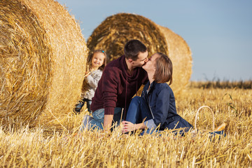 Naklejka na ściany i meble Happy young family with 2 year old girl next to hay bales in harvested field