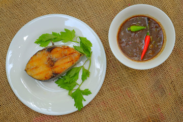 A grilled mackerel fish on white plate served with tamarind sauce is a one of the Malaysian people favorite dish.