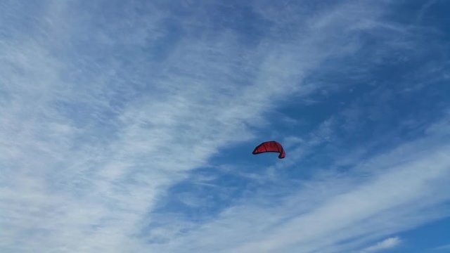 Red paraglider on a background of blue sky with clouds. No sound.