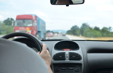 Man driving a car with a dirty front glass after a long drive on a highway and a red truck blurred in front of him