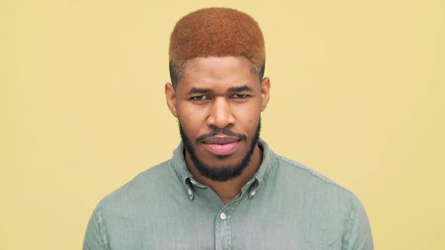 picture of serious metis man with dyed hair in red looking at camera nodding positively then suddenly changing his mind and nodding negatively over yellow background closeup. Concept of emotions