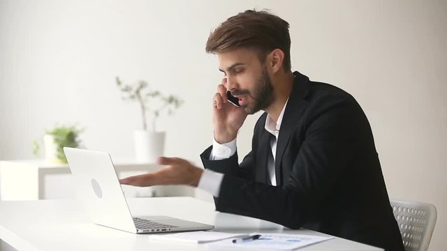 Angry businessman arguing shouting while talking on phone looking at laptop sitting at office desk, dissatisfied client explaining computer problem to customer support, complaining about bad service